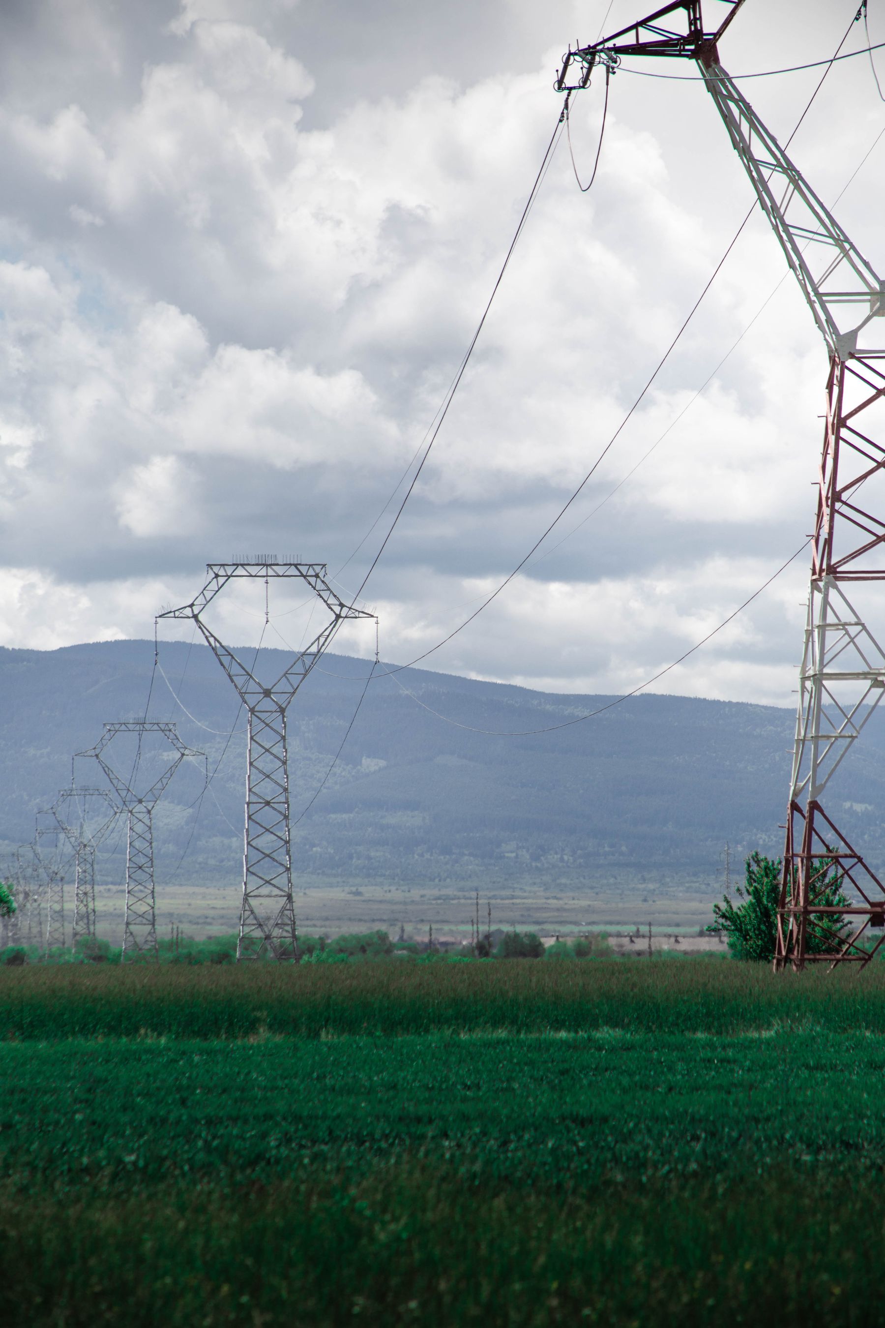 Power lines crossing a green field beneath a cloudy sky.